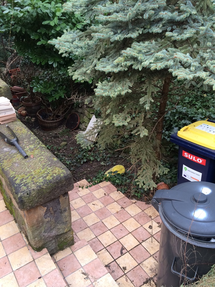 Kertrészlet téglalap alakú, bézs és rózsaszín színű csempékkel burkolt lépcsővel, körülötte növényzettel és kukákkal.